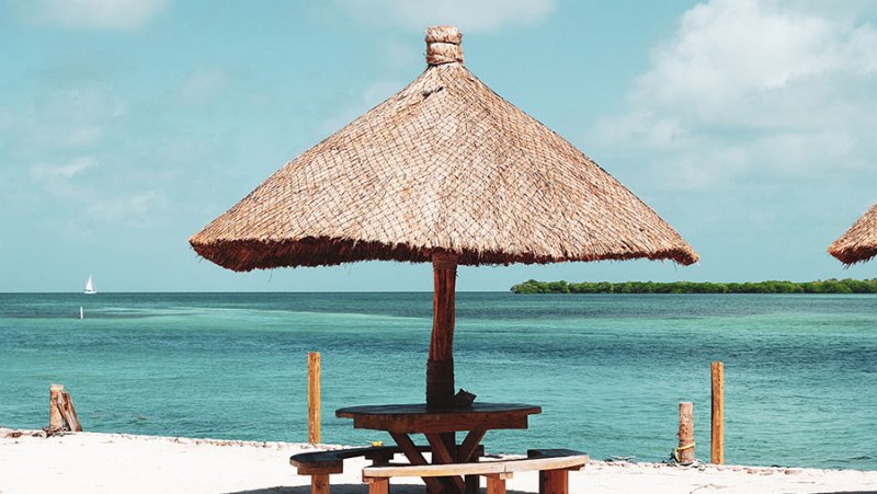 Sonnenschirm am weißen Strand vor türkisfarbenem Meer