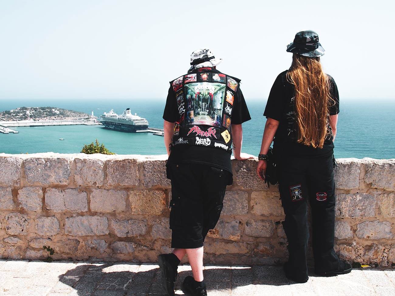 Zwei Menschen vor Steinmauer in Rock T-Shirts mit Blick auf das Meer