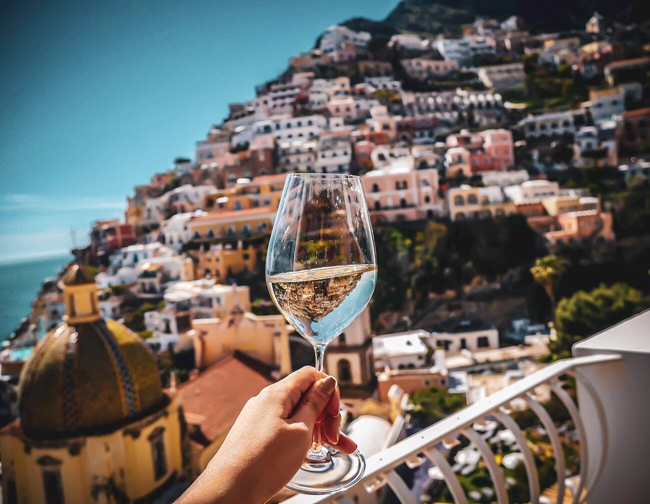 Frau hält Weinglas mit Weißwand vor die Kulisse von Positano